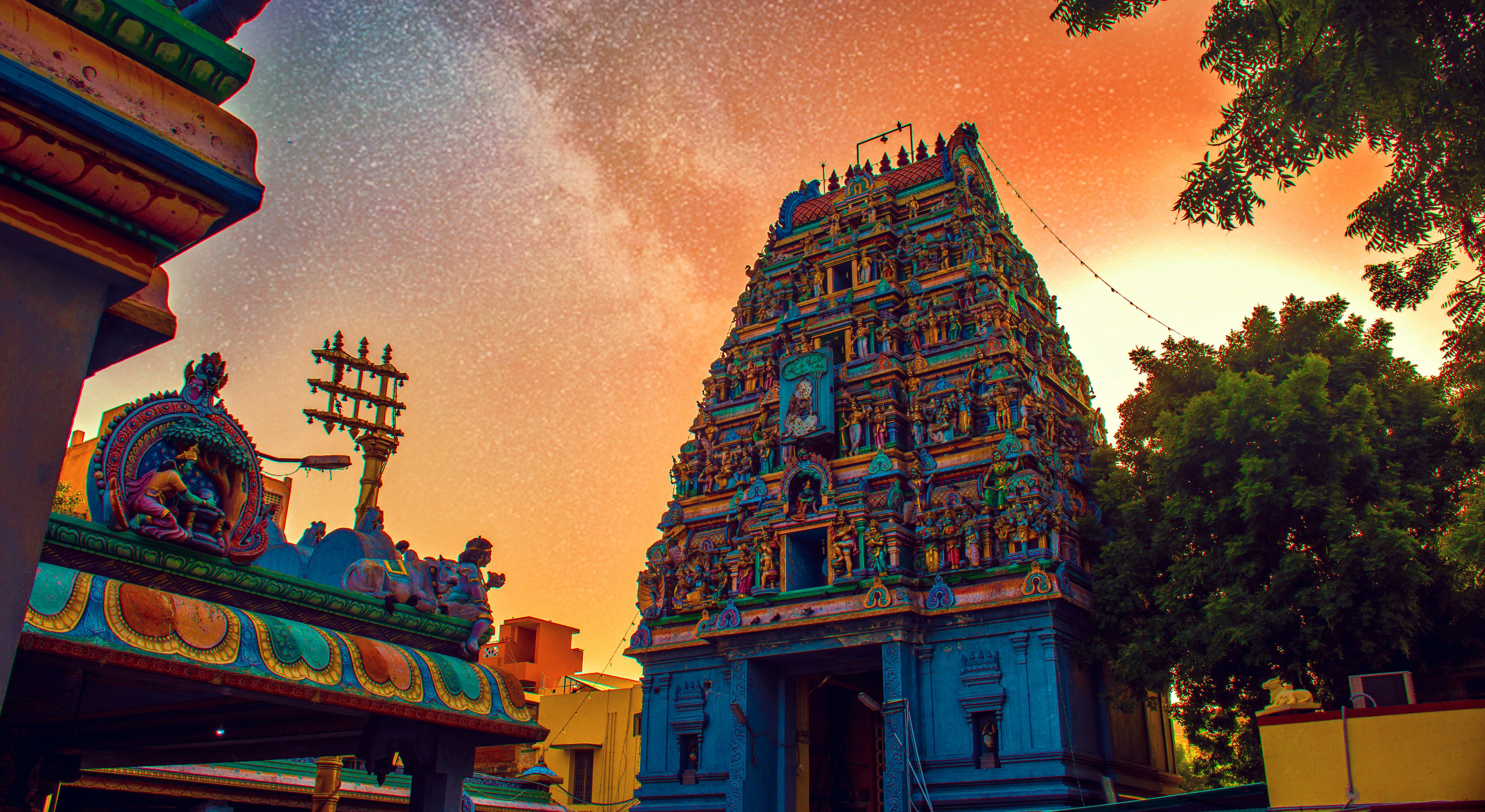 surrounding buildings and trees flanking full view of colorful temple in Tamil Nadu, India during bright sunset